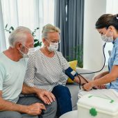 Nurse in medical uniform measuring blood pressure of elderly senior retired patient at checkup meeting at home. Skilled caregiver visiting middle aged woman, geriatric help concept.