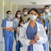 Portrait of a happy doctor leading a group of patients wearing facemasks at the hospital and looking at the camera â COVID-19 pandemic concepts