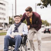 Young man pushing happy senior man in wheelchair