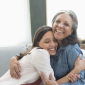 Hispanic mother and daughter hugging on sofa