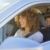 A woman driving in a car with a little boy in the backseat in a car seat.