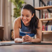 Young girl training at home, doing plank and watching videos on laptop